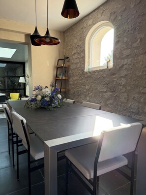 Un espace repas avec un mur en pierre, une fenêtre donnant sur un paysage agréable et une table entourée de chaises.