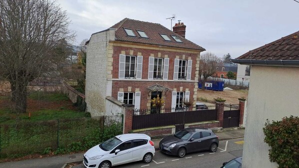 Une maison à deux étages avec une façade en briques, un porche à l’avant et une cour clôturée.