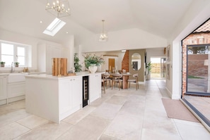 A spacious kitchen with a central island, a dining area with a brick wall, and a large sliding glass door leading to an outdoor area. - The Smithy - Luxury Barn Conversion Cottage Malton & York, Sleeps 6 (Ryton)
