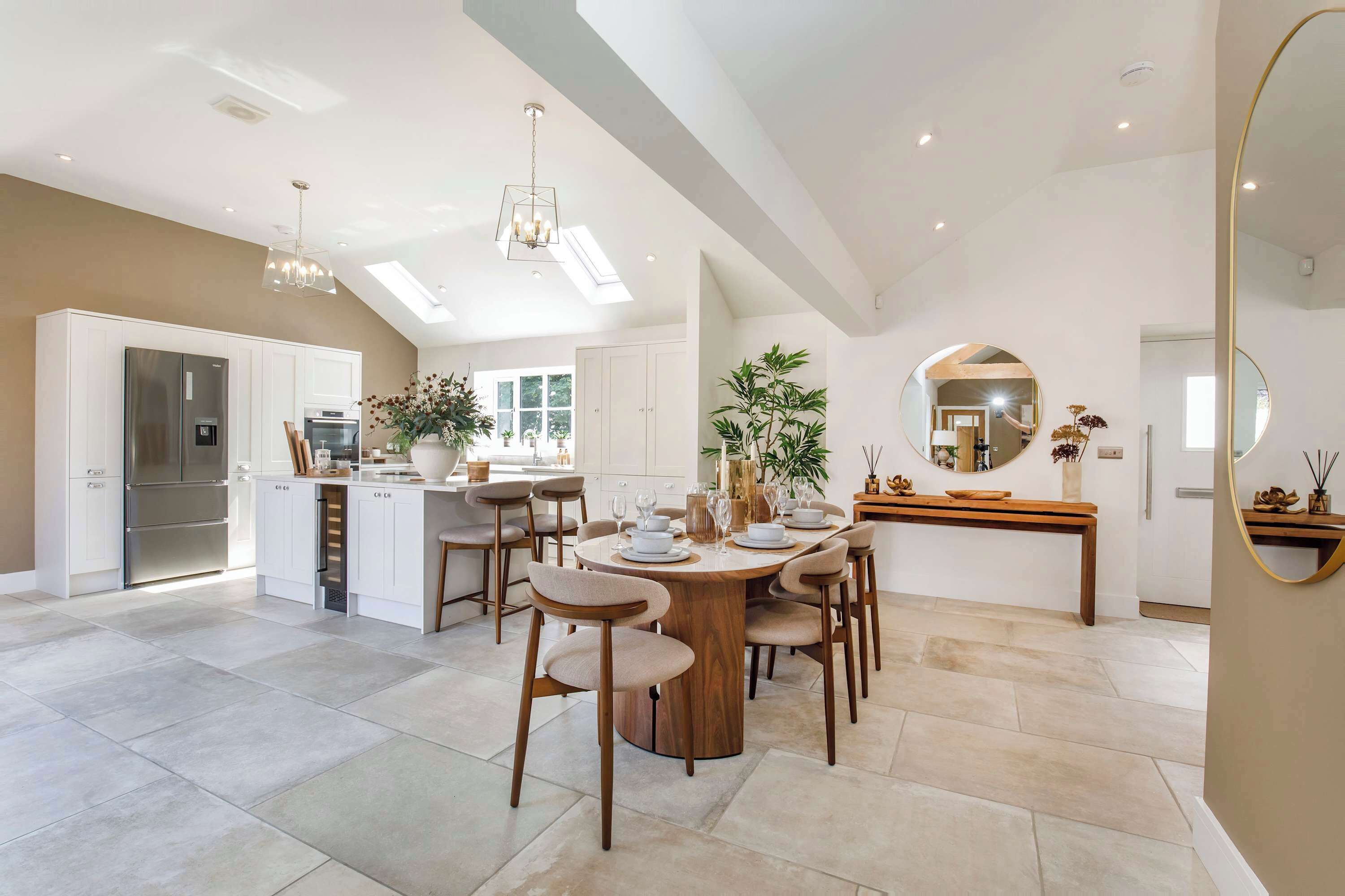 A modern kitchen with a built-in refrigerator, a dining area with a round table and chairs, and a large mirror on the wall.