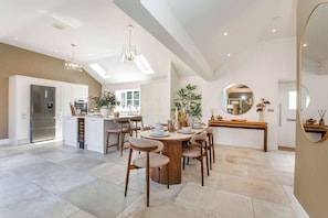 A modern kitchen with a built-in refrigerator, a dining area with a round table and chairs, and a large mirror on the wall. - The Smithy - Luxury Barn Conversion Cottage Malton & York, Sleeps 6 (Ryton)