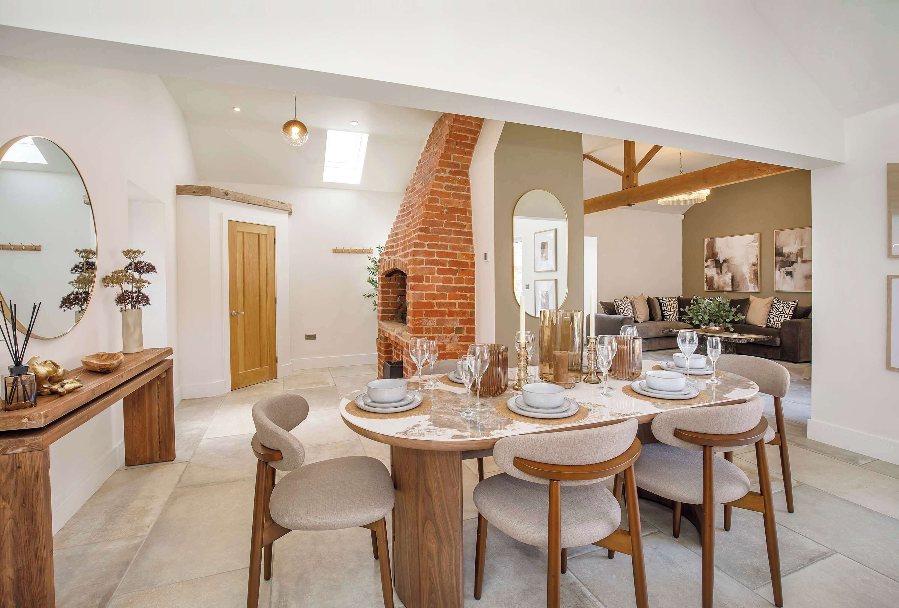 Een eetgedeelte met een schouw van baksteen, een ronde tafel gedekt voor vier personen, en een moderne keuken op de achtergrond.