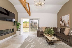 Una sala de estar moderna con chimenea, un amplio sofá, una mesa de centro y un televisor montado en la pared.