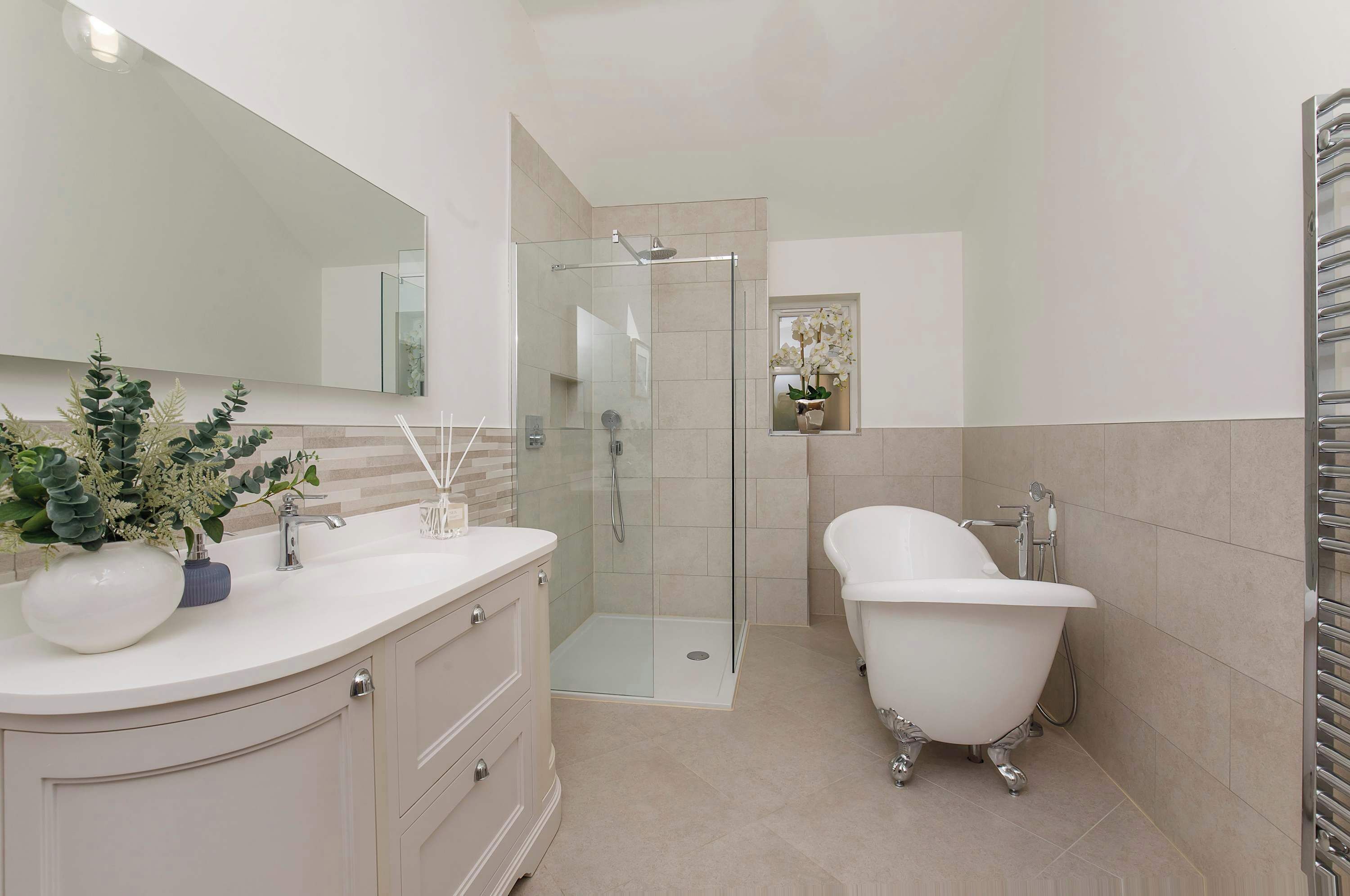 Une salle de bain moderne dotée d’une douche à parois de verre, d’une baignoire sur pieds et d’un meuble-lavabo avec un miroir et un vase de fleurs.
