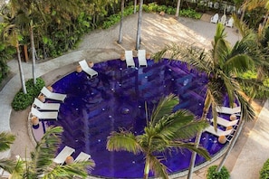 Une piscine à débordement circulaire, entourée de chaises longues, de palmiers et de verdure.