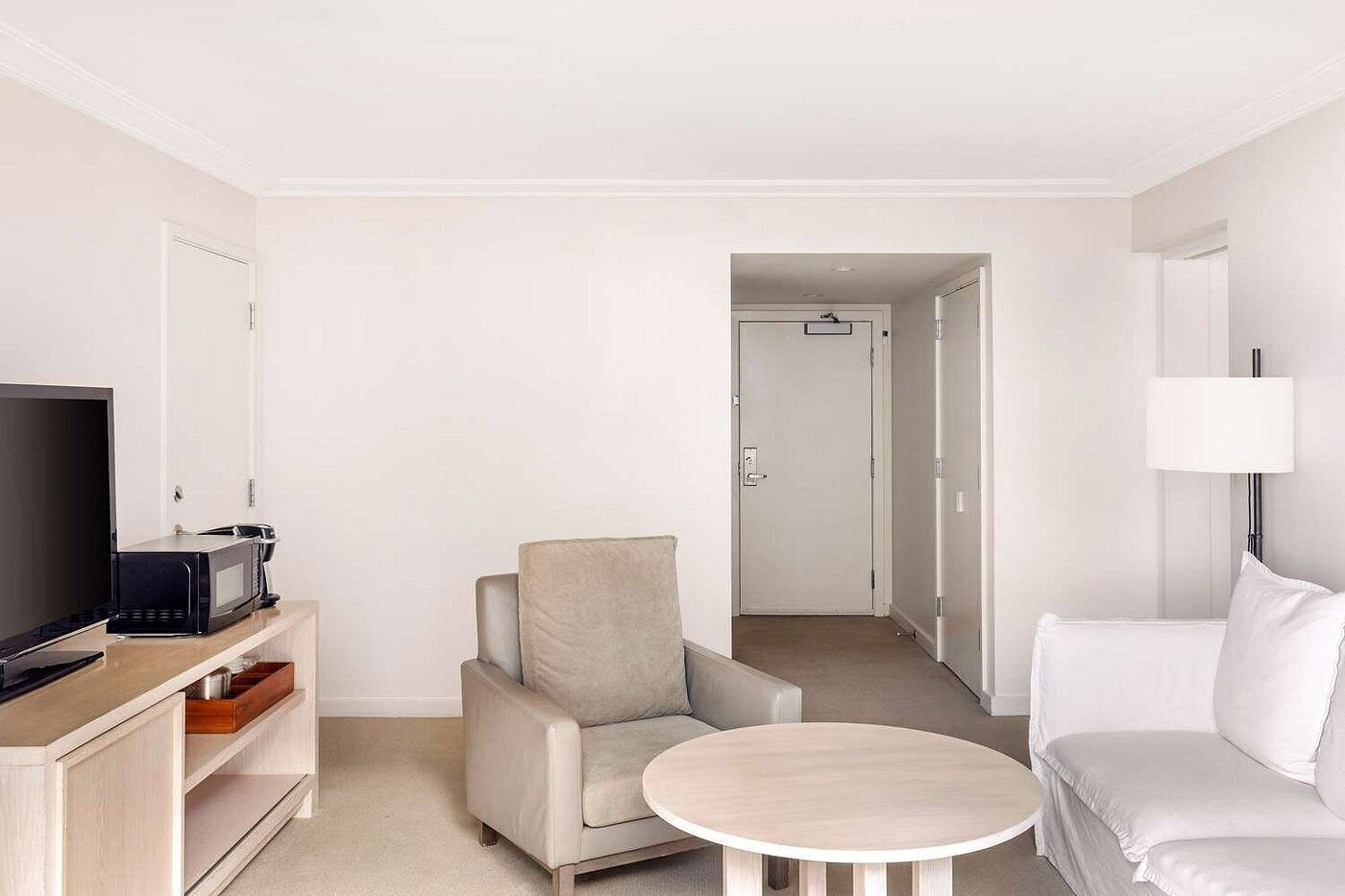 A hotel room with a flat-screen TV, a microwave, a sofa, a chair, and a small round table.