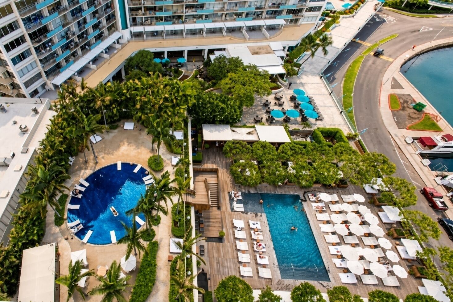 Un hotel con una amplia piscina exterior, varias zonas de descanso y un aparcamiento.
