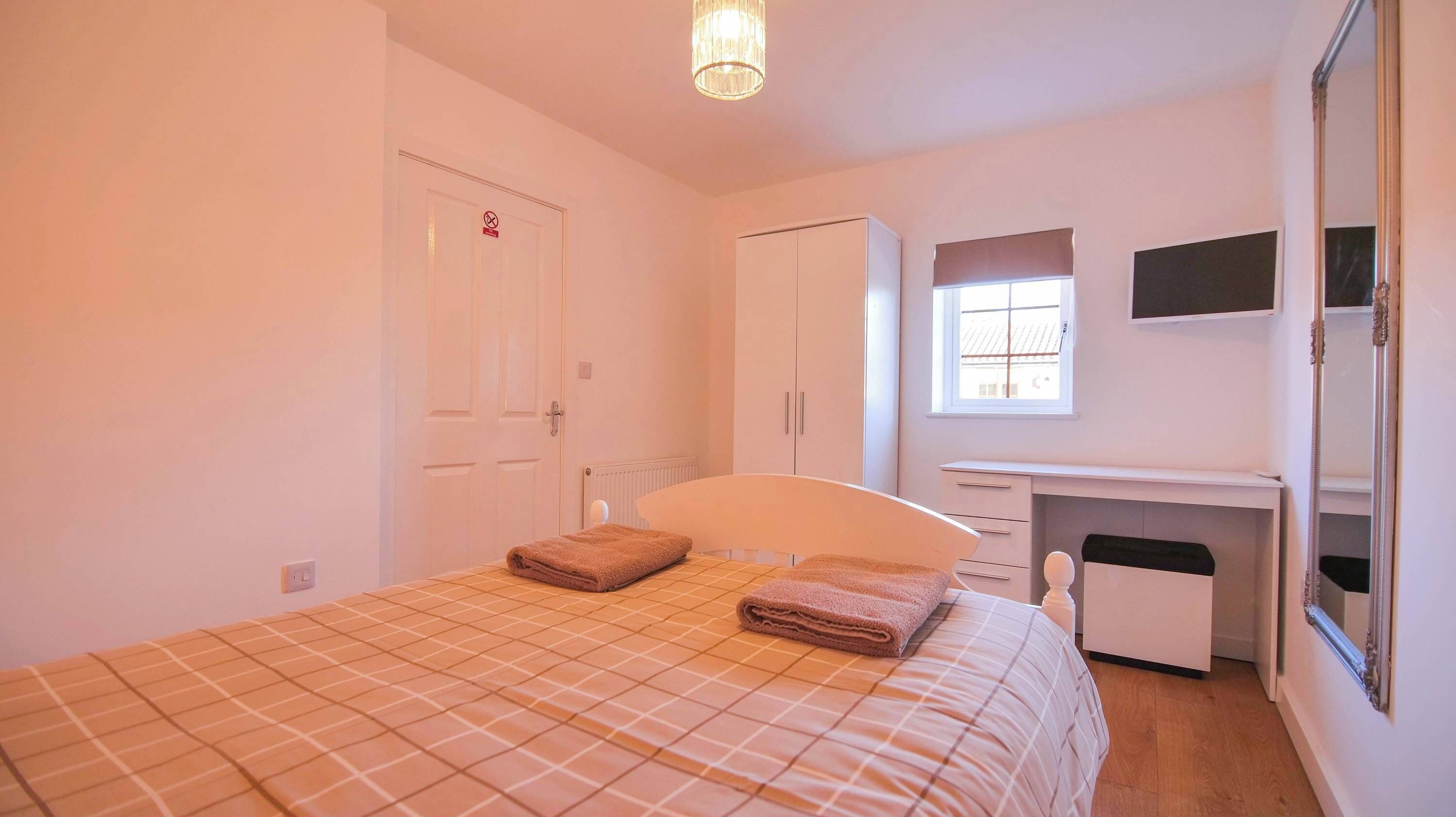 A bedroom with a bed, a desk, a wardrobe, and a window.