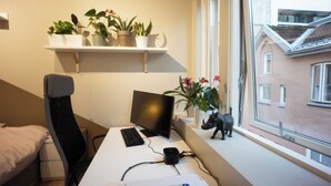 A bedroom with a bed, a desk with a computer, a window, and a shelf with plants. - Spacious, High-End Loft Apartment in the City Center (Unknown)