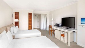 Ett hotellrum med två sängar, ett skrivbord med en tv, en stol och en lampa.