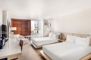 Une chambre d’hôtel avec deux lits, un bureau, une chaise, une télévision et une fenêtre avec des stores.