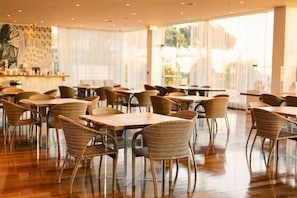 A spacious indoor dining area with wicker chairs and tables, large windows, and a modern interior design.