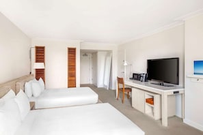 Una habitación de hotel con dos camas, un escritorio con televisor, una silla y una lámpara.