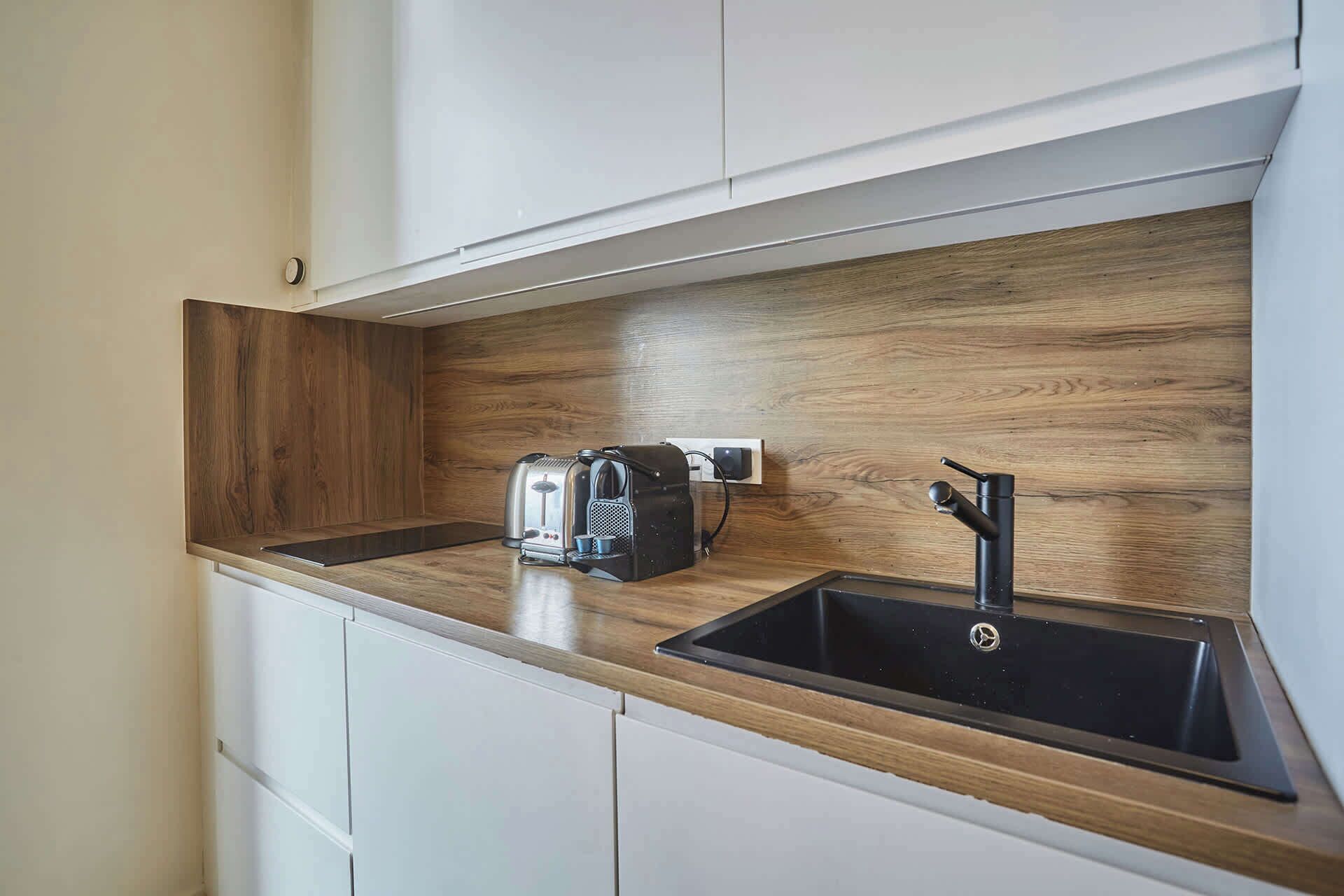A kitchen with a wooden countertop, a coffee machine, and a black sink.
