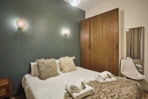 Ein Schlafzimmer mit einem Bett, weichen Kissen, einem Holzschrank, einem Sessel und einem Spiegel.