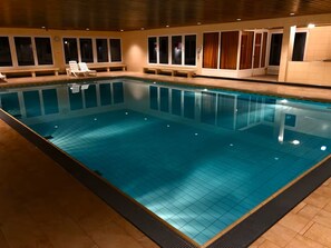 A rectangular indoor swimming pool with a tiled floor and walls, surrounded by windows and benches. - Almherzl - Indoor pool, sauna, mountain views, skiing, renovated (Missen-Wilhams)