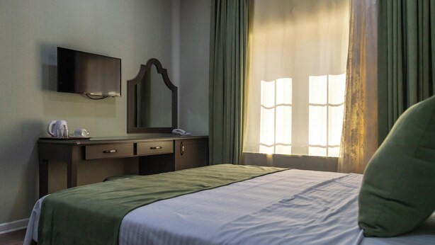 A hotel room with a bed, a bedside table, a mirror, a flat-screen TV, and a window with curtains.
