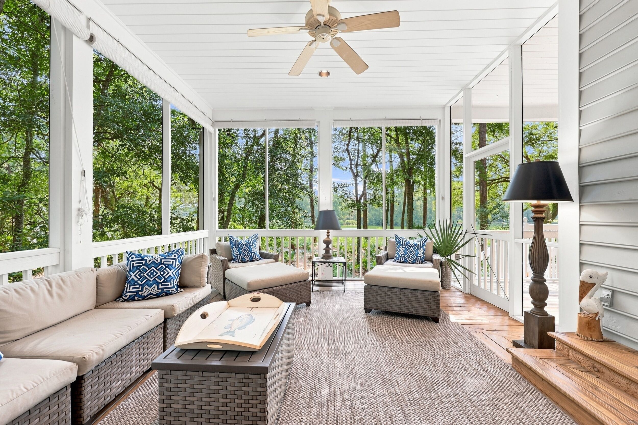 A covered porch with wicker furniture, a ceiling fan, and a view of trees.
