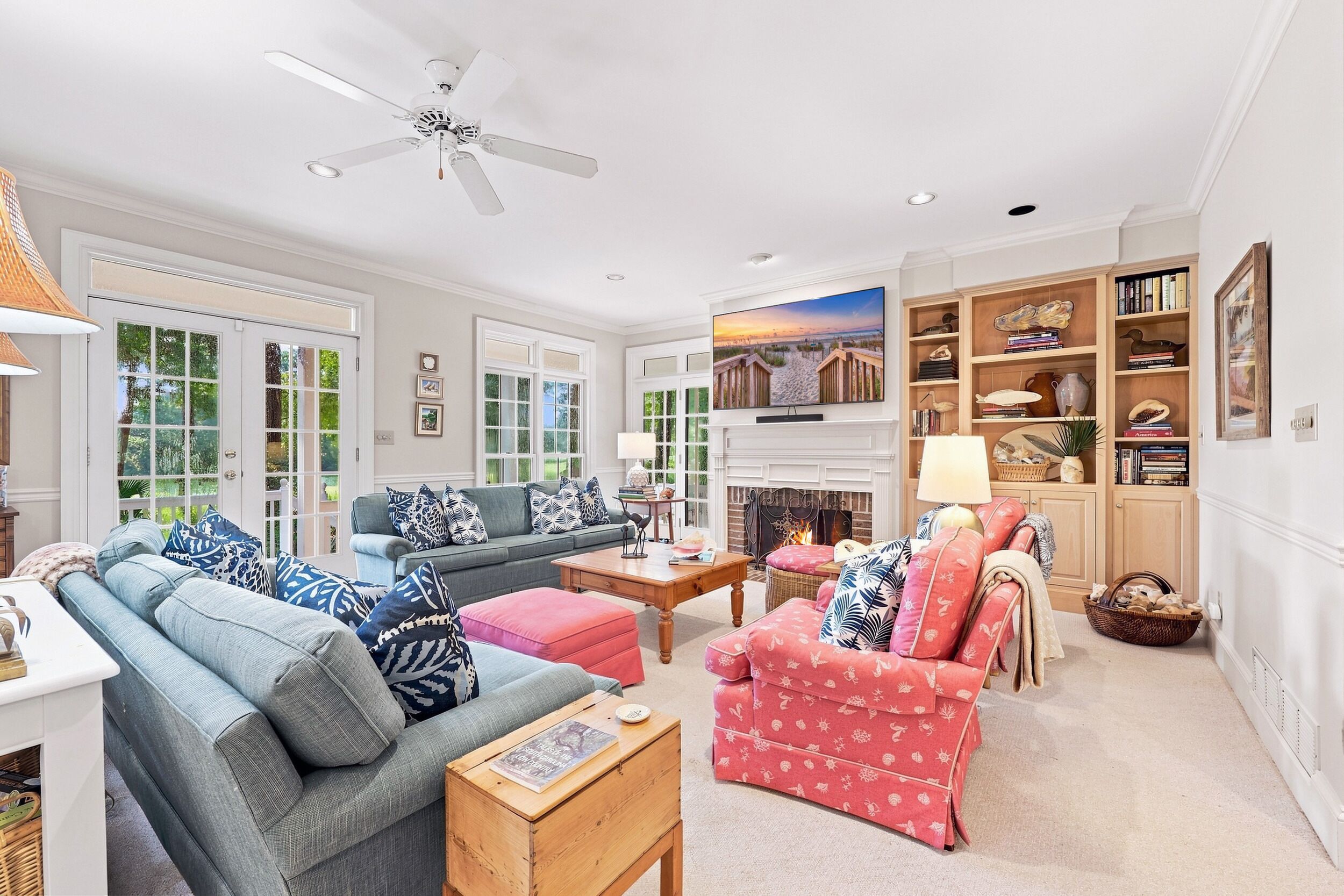 A spacious living room with a fireplace, a ceiling fan, and a large window overlooking a garden.