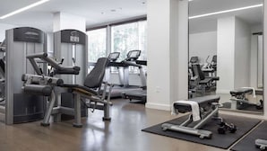 Une salle de sport moderne équipée de machines de cardio, de postes d’entraînement avec poids et d’un grand miroir.
