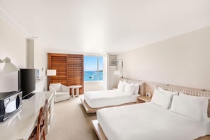 Een hotelkamer met twee bedden, een televisie, een bureau en uitzicht op zee.