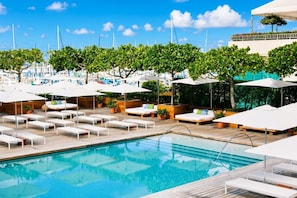 Un espace aménagé au bord de la piscine, avec des chaises longues, des parasols et une piscine à l’eau d’un bleu limpide.