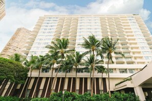 Un hôtel à plusieurs étages doté de balcons, de palmiers et surplombant un ciel dégagé.