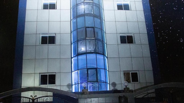 A multi-story building with a central glass elevator shaft, a gated entrance with decorative ironwork, and a clear night sky. - Champion Hotel (DOUALA)