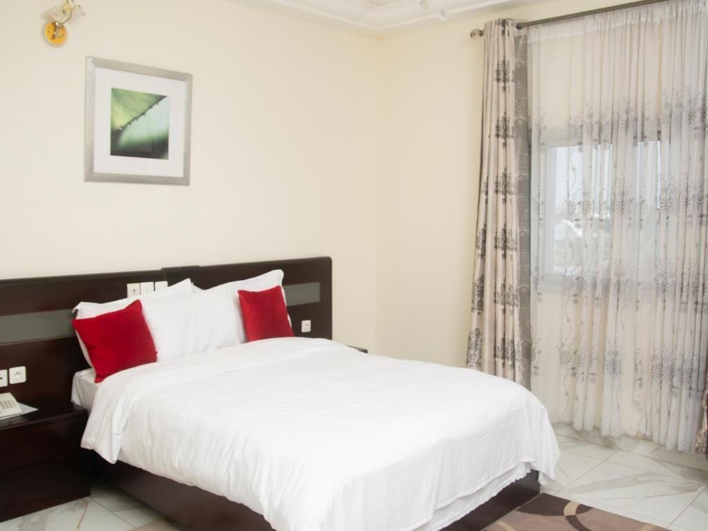 Une chambre d’hôtel avec un lit, une table de chevet, un tableau encadré au mur et une fenêtre avec des rideaux.