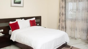 A hotel room with a bed, a nightstand, a framed picture on the wall, and a window with curtains. - Champion Hotel (DOUALA)
