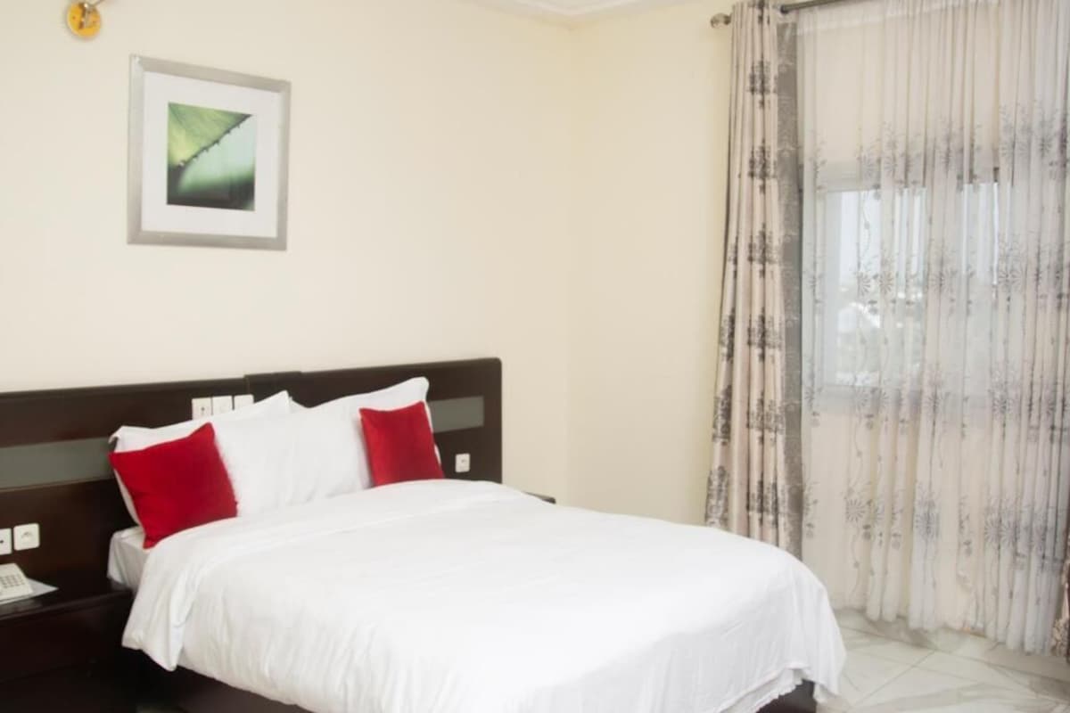 Une chambre d’hôtel avec un lit, une table de chevet, un tableau encadré au mur et une fenêtre avec des rideaux.