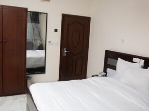 Habitación de hotel con cama, armario, puerta y espejo.