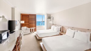 Ett hotellrum med två sängar, en TV, ett skrivbord och utsikt över havet.