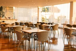 A spacious indoor dining area with wicker chairs and tables, large windows, and a modern interior design.