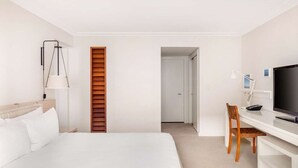 Une chambre d’hôtel comprenant un lit, un bureau avec une chaise, une télévision et une porte donnant sur une autre pièce.