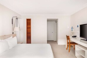 A hotel room with a bed, a desk with a chair, a television, and a door leading to another room.