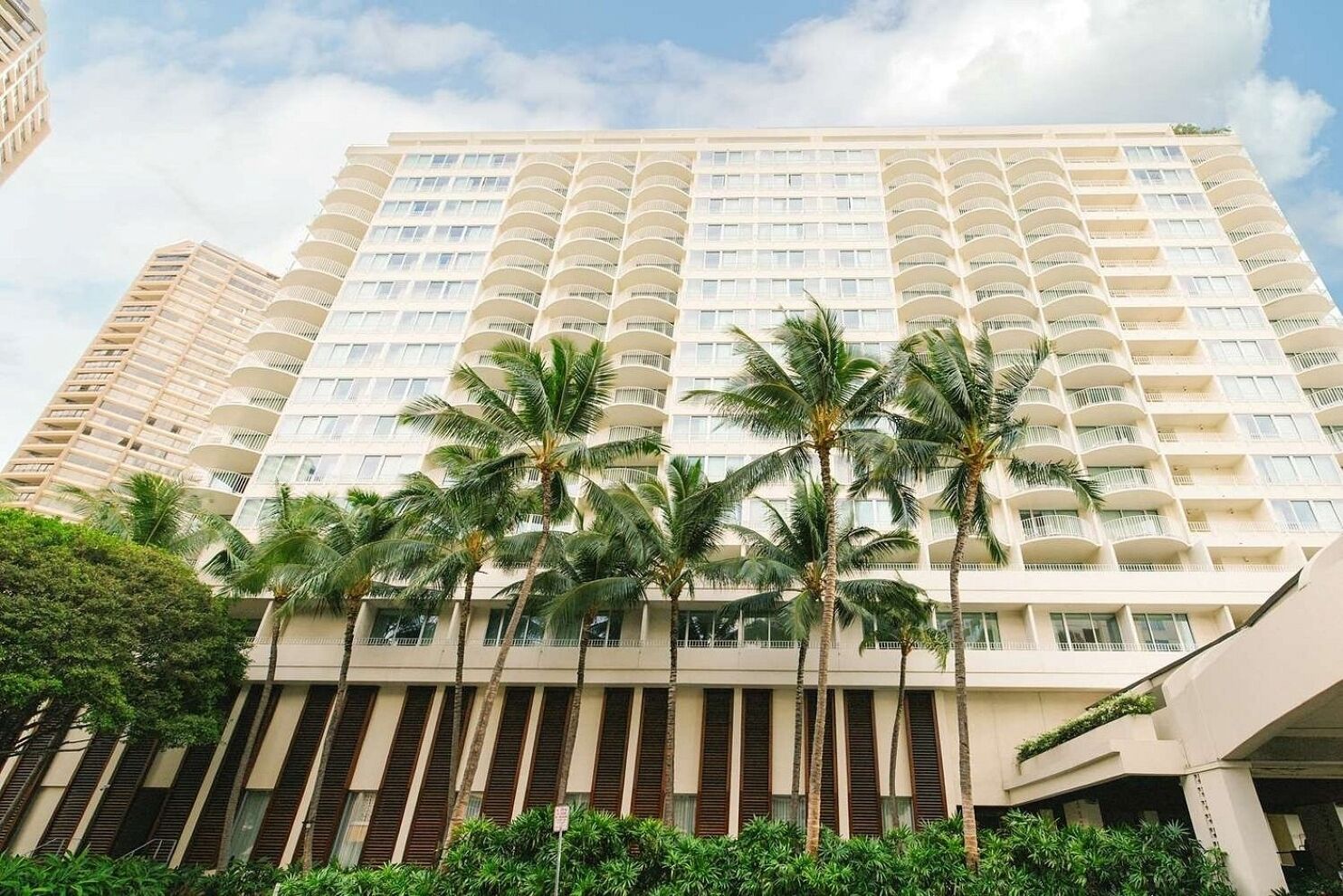 Un hotel de varios pisos con balcones, palmeras y un cielo despejado.