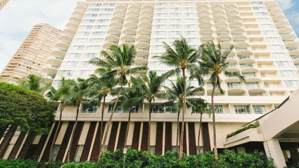 Un hôtel à plusieurs étages doté de balcons, de palmiers et surplombant un ciel dégagé.