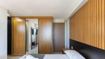 A modern hotel room with a bed, a wooden panel wall, a wardrobe, and a bathroom with a mirror and towel rack.