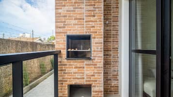 Un balcón con un muro de ladrillo, una pequeña chimenea y un ventanal corredera.