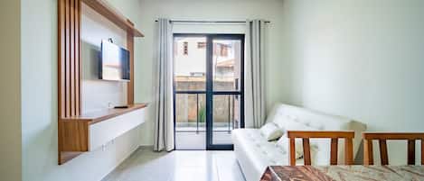 Una habitación moderna con sofá, televisor montado en un panel de madera, mesa de comedor y puerta corrediza de vidrio que da a un espacio exterior.