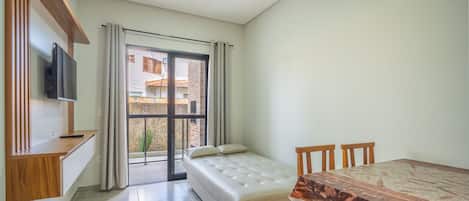 A small, modern room with a bed, a TV mounted on the wall, and a dining table.