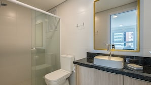 Un baño moderno con cabina de ducha de vidrio, inodoro blanco, lavabo con encimera negra y un espejo grande con marco dorado.