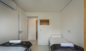 Habitació petita i neta amb dos llits, una prestatgeria de fusta sobre la porta i una paret blanca.