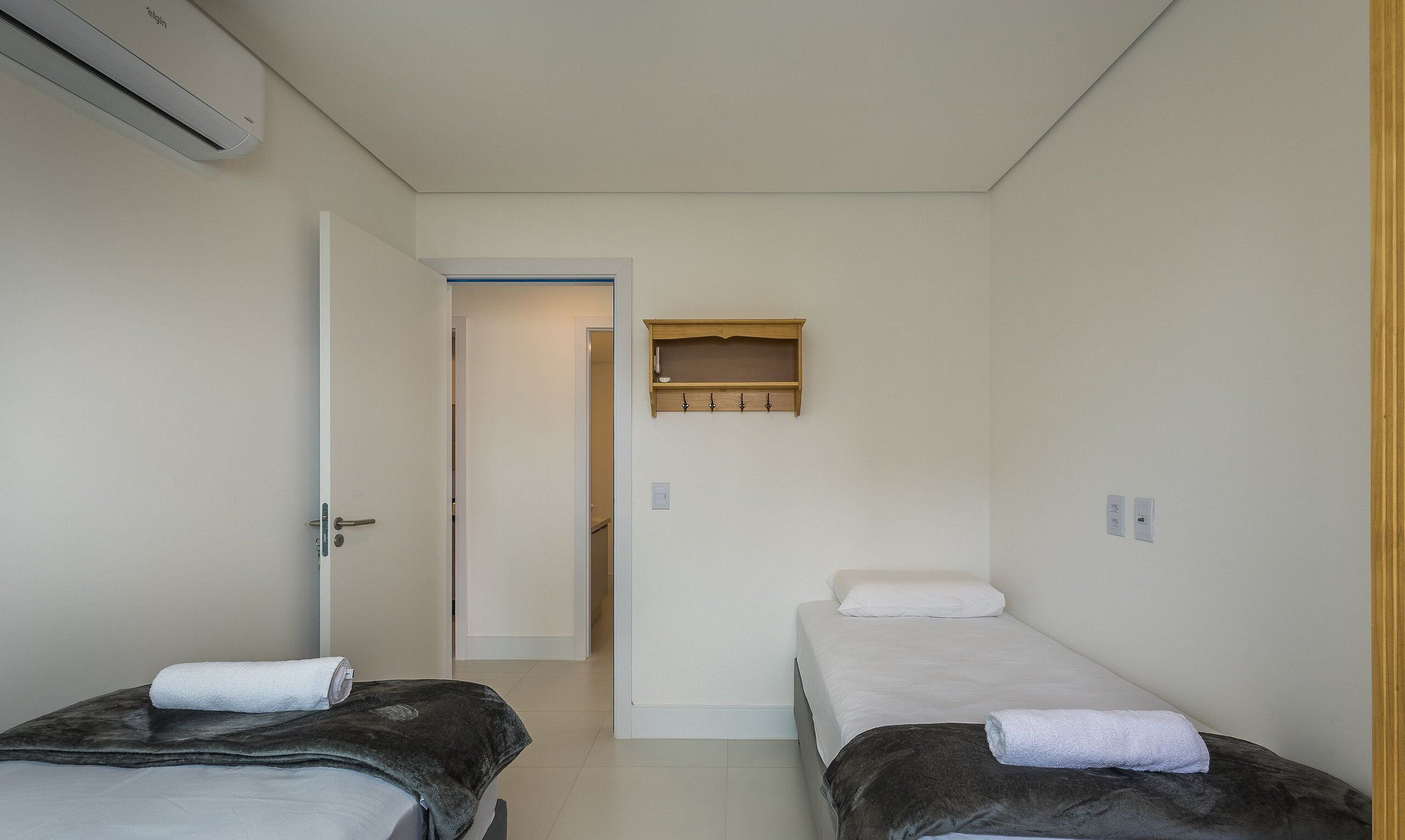 A small, clean room with two beds, a wooden shelf above the door, and a white wall.