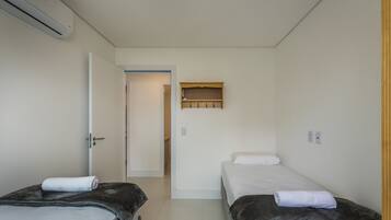 A small, clean room with two beds, a wooden shelf above the door, and a white wall.