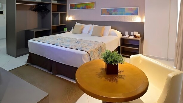 Ein modernes Hotelzimmer mit einem großen Bett, einer Sitzecke mit Tisch und einem eingebauten Kleiderschrank.