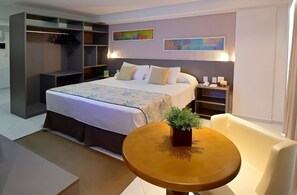 A modern hotel room with a large bed, a seating area with a table, and a built-in wardrobe. - Elegant Suite Just Steps from Cabo Branco Beach - Near Cabo Branco Lighthouse (Paraíba)