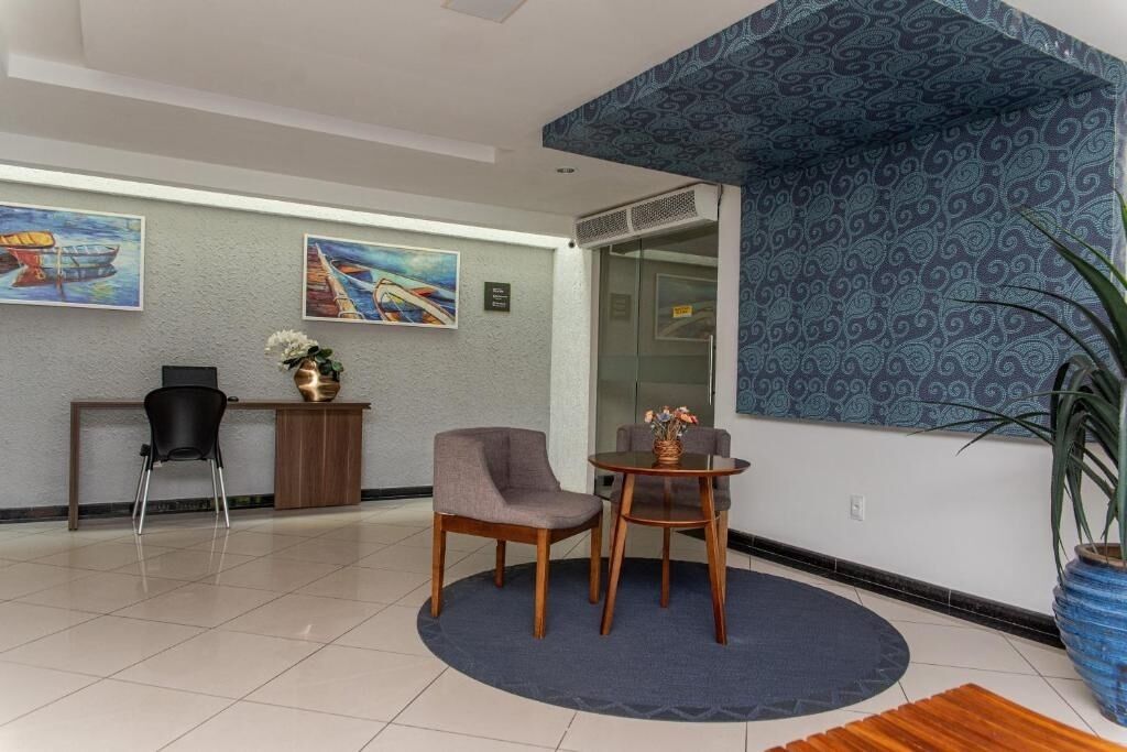A reception area with a reception desk, two chairs, a small table with a vase, and two paintings on the wall.