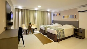 Ein Hotelzimmer mit zwei Betten, einem Schreibtisch, einem Stuhl, einem Fernseher und einem Fenster mit Vorhängen.